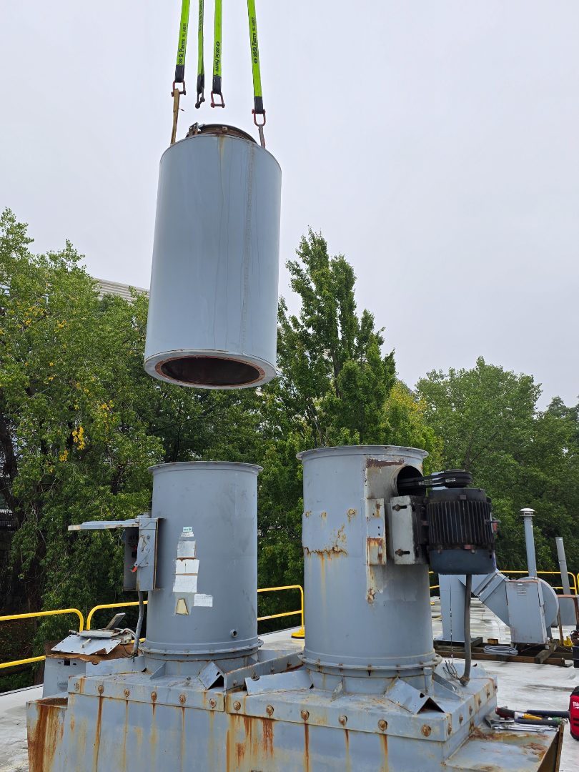 An exhaust fan stack on four rigging slings, flying in above the roof