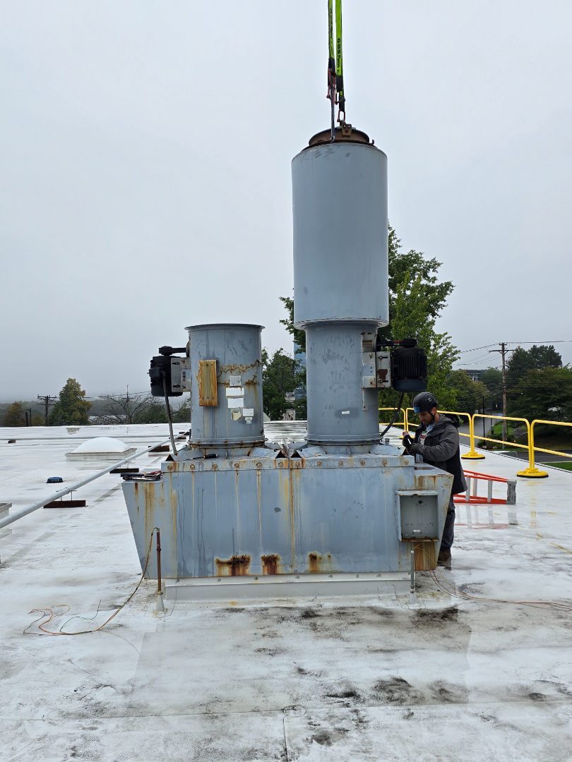 A single new exhaust stack standing on its curb with a worker at the roof rail